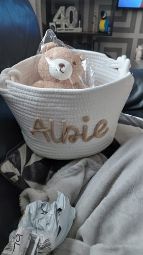 Customer's white personalized knitted basket with the name 'Albie' embroidered on the front, holding a small teddy bear.
