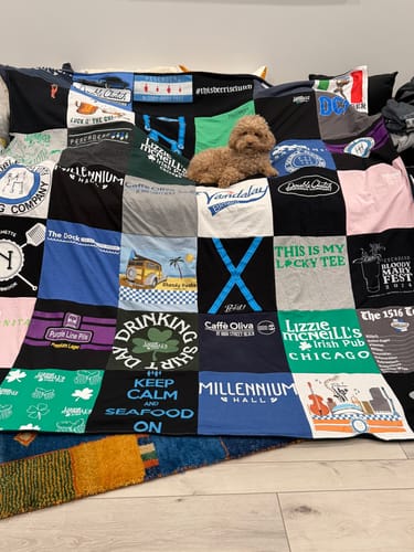 Customer's colorful Premium T-Shirt Quilt displayed on a couch, with a small dog resting comfortably on top.
