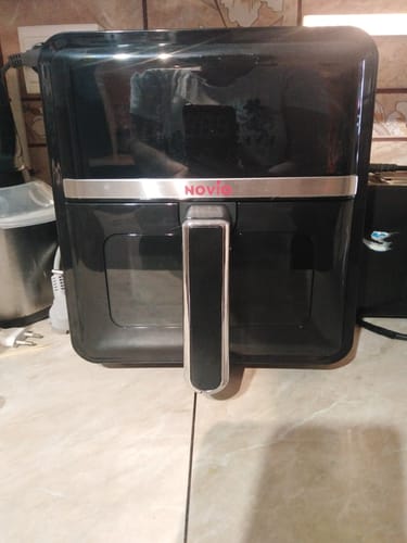Recenzentul prezintă friteuza neagră Air Fryer Novio StonePro pe un blat de bucătărie.