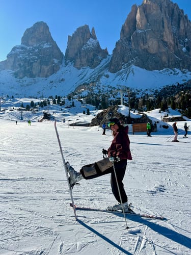 Reviewer on a ski slope lifting one leg to show the baggy fit of the black color-block snow pants.