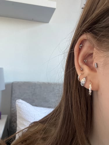 Close-up of a customer's ear showing the silver Selene huggies worn in the second piercing as part of an ear stack.
