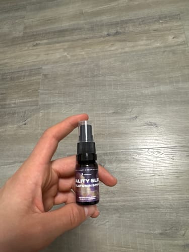 Customer holding the small bottle of Melatonin Sleep Spray against a wood-grain background.