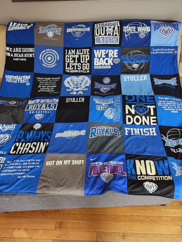 Customer's finished Premium T-Shirt Quilt made from blue, black, and grey volleyball-themed shirts spread across a couch.