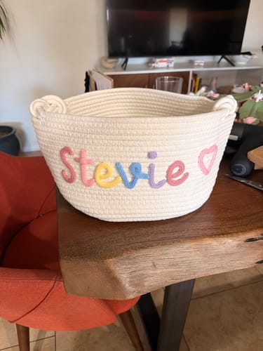 Reviewer's off-white knitted basket personalized with the name 'Stevie' in multicolor yarn and a pink heart icon.