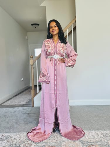 Customer wearing the long, pink Caftan Sania with its decorative belt in a hallway.