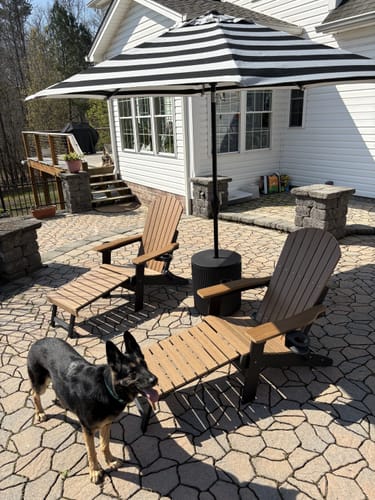 Customer's two Folding Adirondack Chairs on a patio with the built-in footrests extended and a dog nearby.
