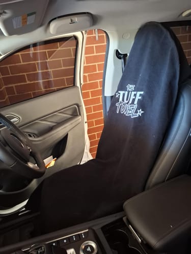 Reviewer's black Waterproof Car Towel Seat Cover protecting a leather driver's seat in a car.
