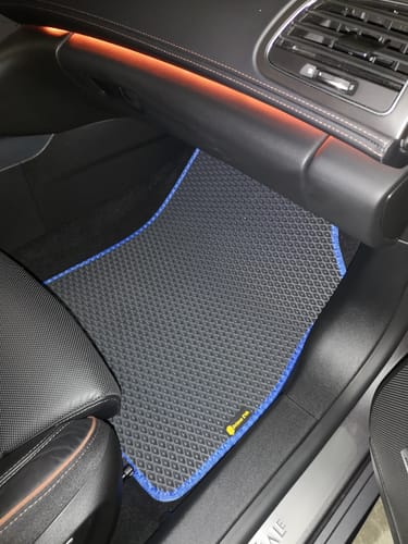 Recenzent pokazuje czarny dywanik samochodowy z niebieskim obszyciem, idealnie dopasowany do podłogi po stronie pasażera.