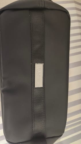Reviewer's black toiletry bag, showing a close-up of the central strap and metal plate.