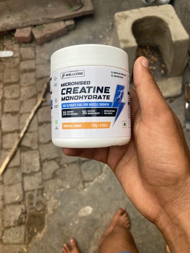 Customer's hand holding a white jar of Wellcore Micronised Creatine Monohydrate supplement outdoors.