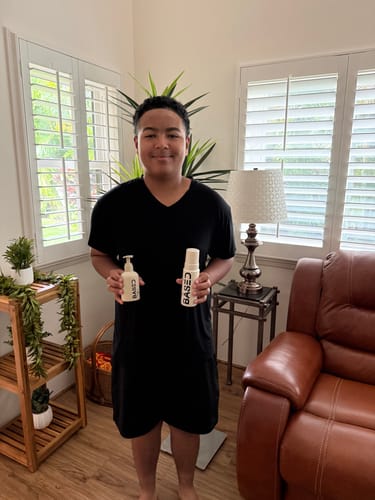 A young reviewer smiling while holding the two bottles from the Shower Duo bundle at home.