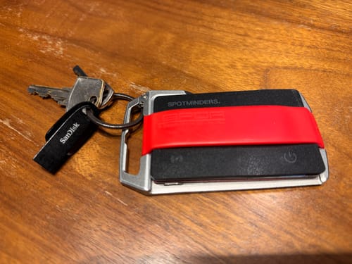 Customer's SPOTMINDERS Tracking Card in a key holder with a red strap, shown with keys on a wooden surface.
