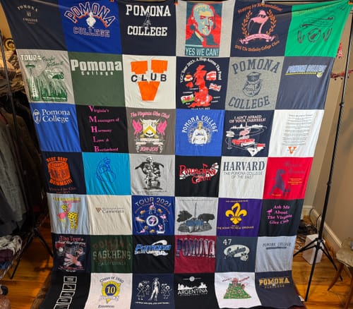 Customer's large Premium T Shirt Quilt made from many colorful college-themed t-shirts, hanging on a stand.