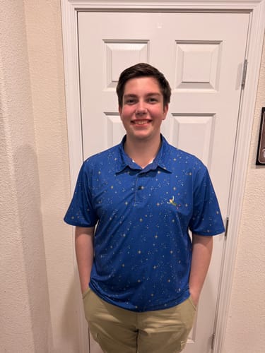 Customer smiling while wearing the blue Peter Pan 'Second Star to the Right' All-Day Polo indoors.