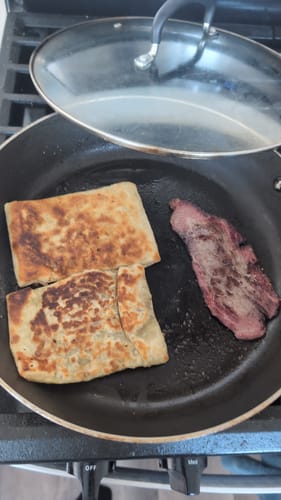Customer cooking a slice of Halal Sliced Pastrami in a black frying pan with two flatbreads.