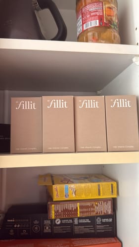 תמונת לקוח של ארבע קופסאות של תוסף השיער Fill it מסודרות על מדף בארון.