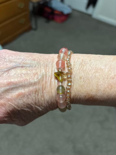 Close-up of a reviewer wearing the pink mix quartz Faithfully Bracelet, stacked with another beaded bracelet on their wrist.