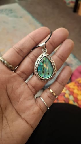 Close-up of a customer's hand holding a teardrop necklace with an iridescent abalone shell.