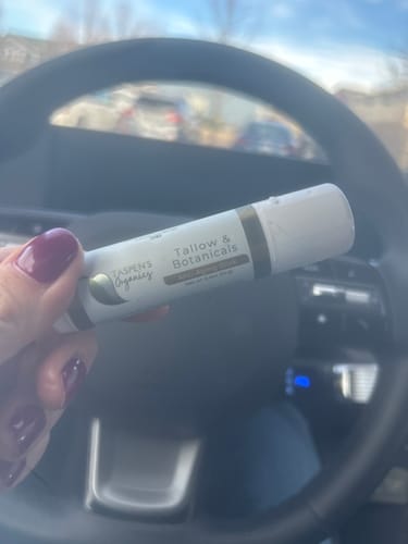 Customer holding the Tallow & Botanicals Salve Stick in their hand inside a car, showing the product label.