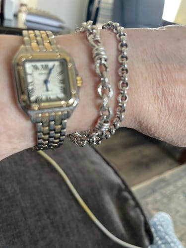 Close-up of a reviewer's wrist wearing a two-tone Clarine watch next to two silver bracelets.