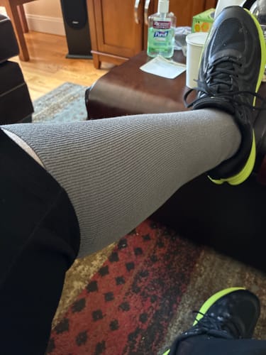 A reviewer's leg wearing a grey Performance Eucalyptus Compression Sock with a black athletic shoe.