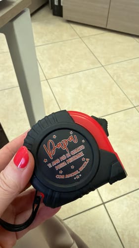 Ein Rezensent hält das personalisierte rot-schwarze Maßband in der Hand.