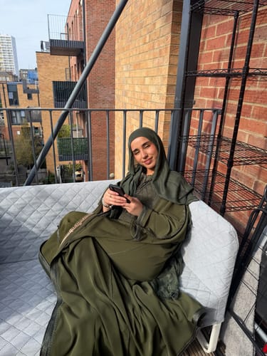 Reviewer sitting on a balcony sofa wearing the flowing Daur Olive Green kimono with matching hijab.