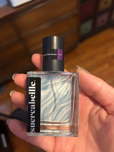 Customer holding a clear bottle of Velvet Frost perfume, showing the light blue and white swirled liquid inside.