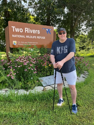 Reviewer wearing a dark gray T.V.P. Essential Tee while standing with trekking poles at a wildlife refuge.