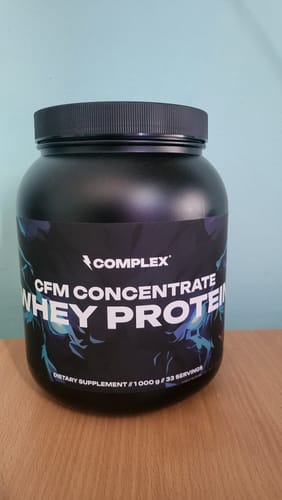 Customer's black tub of Complex CFM Whey Protein sitting on a wooden table.