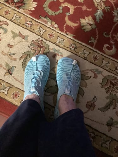 Reviewer standing in light blue Nova Splash barefoot boots on a patterned rug.
