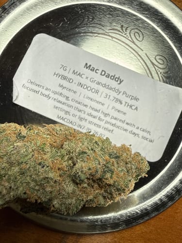 Reviewer's close-up of a dense Mac Daddy flower bud on a silver tray next to the product label.