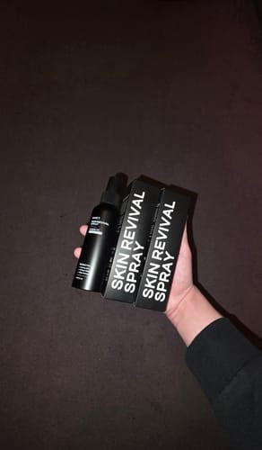 Customer holding a black bottle and two boxes of the Skin Revival Spray.