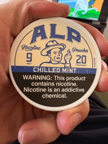 Reviewer's hand holding a round, white tin of ALP Chilled Mint Nicotine Pouches.