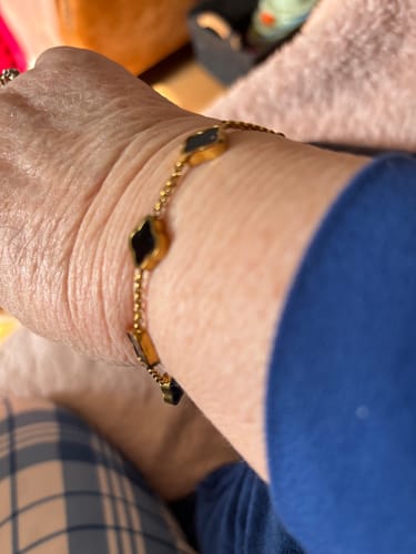 Close-up of a reviewer's wrist wearing the gold Celine Clover Bracelet with black clover motifs.