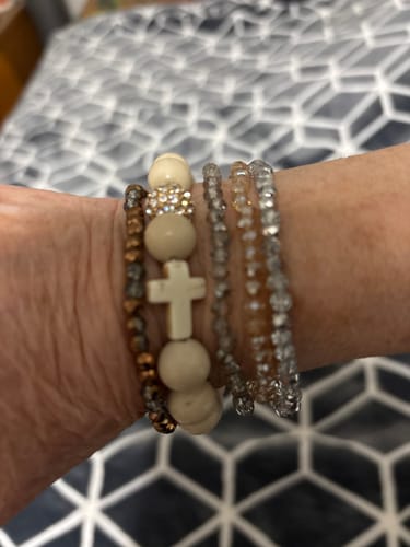 Customer's wrist showing the Crystal Stacker Set layered with a thicker, beaded cross bracelet.