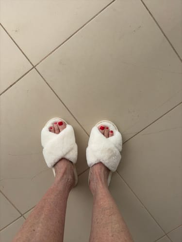 Customer wearing the white, fluffy Nordic Cozy Cross Band Slippers on a tiled floor.