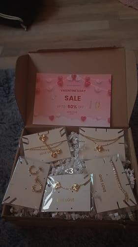Rezensent zeigt liebevoll verpackten Schmuck, darunter mehrere goldfarbene Plain Clover Kette Halsketten in einer Box.