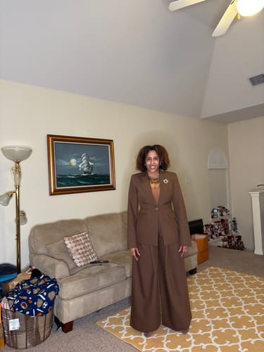 Customer smiling while wearing the brown Power Shoulder Fitted Suit Blazer with matching wide-leg pants indoors.