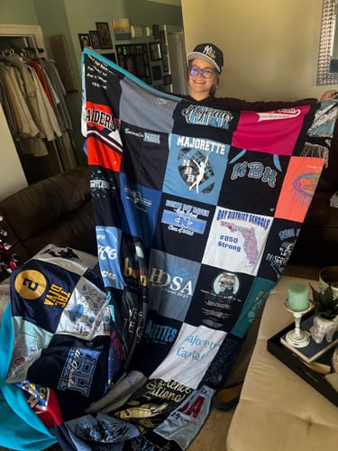 A happy customer holds up her large Project Repat T-Shirt Quilt, showing the patchwork design of various shirts.