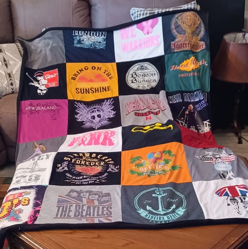 Customer's finished Project Repat T-Shirt Quilt made of many colorful t-shirt squares draped over furniture.