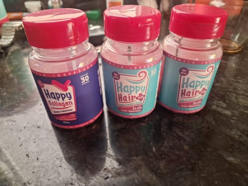 Cliente mostra os três potes recebidos: dois de Happy Hair e um de Happy Collagen, sobre uma bancada escura.