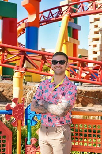 Reviewer wearing the pink patterned 'Rowdy Rex' All-Day Polo in front of a colorful toy-themed ride.