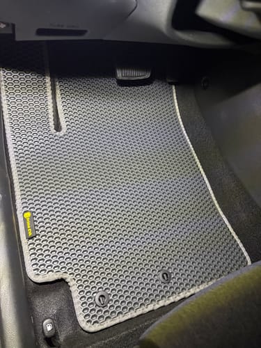 Recenzent pokazuje dopasowaną szarą matę podłogową po stronie kierowcy w swojej Kii.