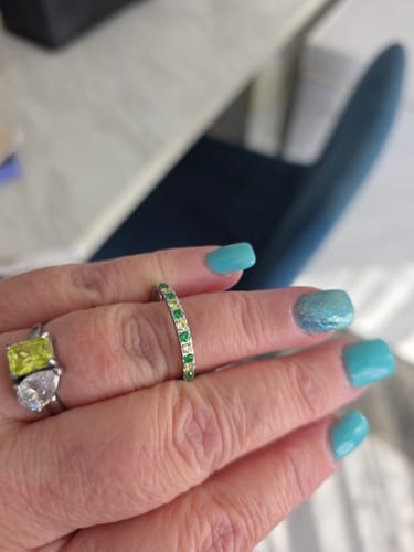 Reviewer's hand wearing the Eterna Birthstone Ring with alternating green and light green stones next to another ring.