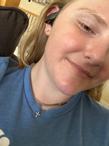 Close-up of a customer wearing the dainty Cascade Cross Necklace layered with another chain against their blue shirt.