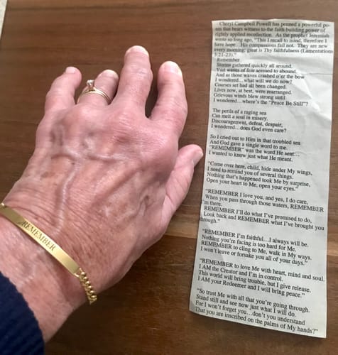 A reviewer's wrist wearing the gold engraved chain bracelet with the word 'REMEMBER' next to a poem.
