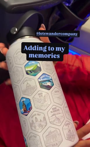 Customer holding the white World Explorer Bottle, with several colorful travel stickers already applied.