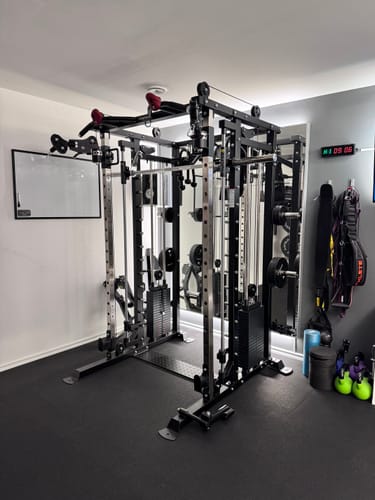 Rezensent zeigt das stabile, schwarze Fortress Multipresse Set, aufgebaut in einem Home Gym.