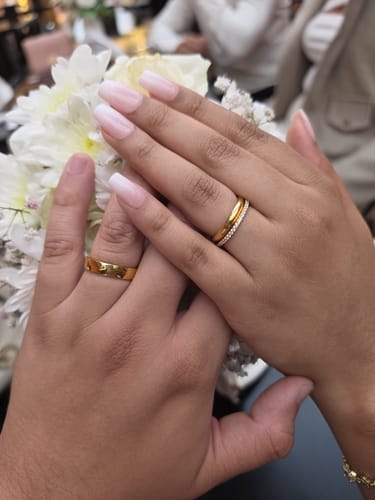 Cliente mostrando las manos de una pareja, cada una con un Anillo Minimal Oro como alianza de matrimonio sobre flores.
